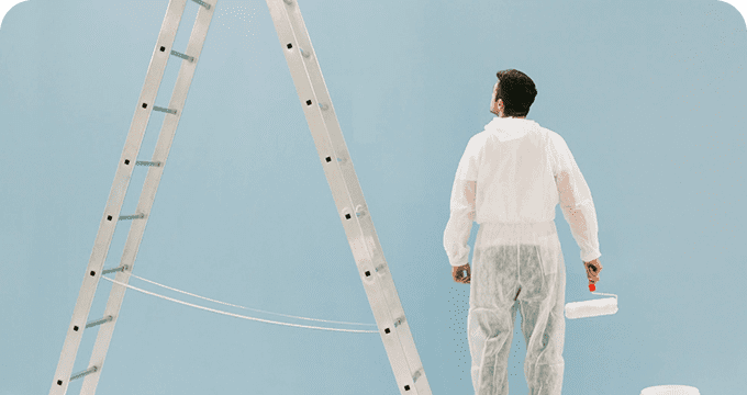 A man in white overalls standing next to a ladder.
