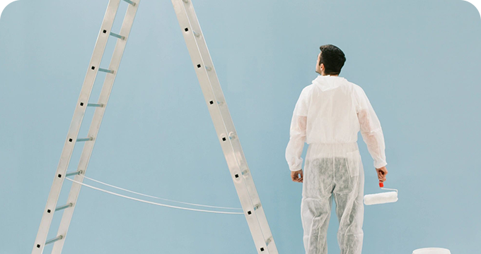 A man in white overalls standing next to a ladder.